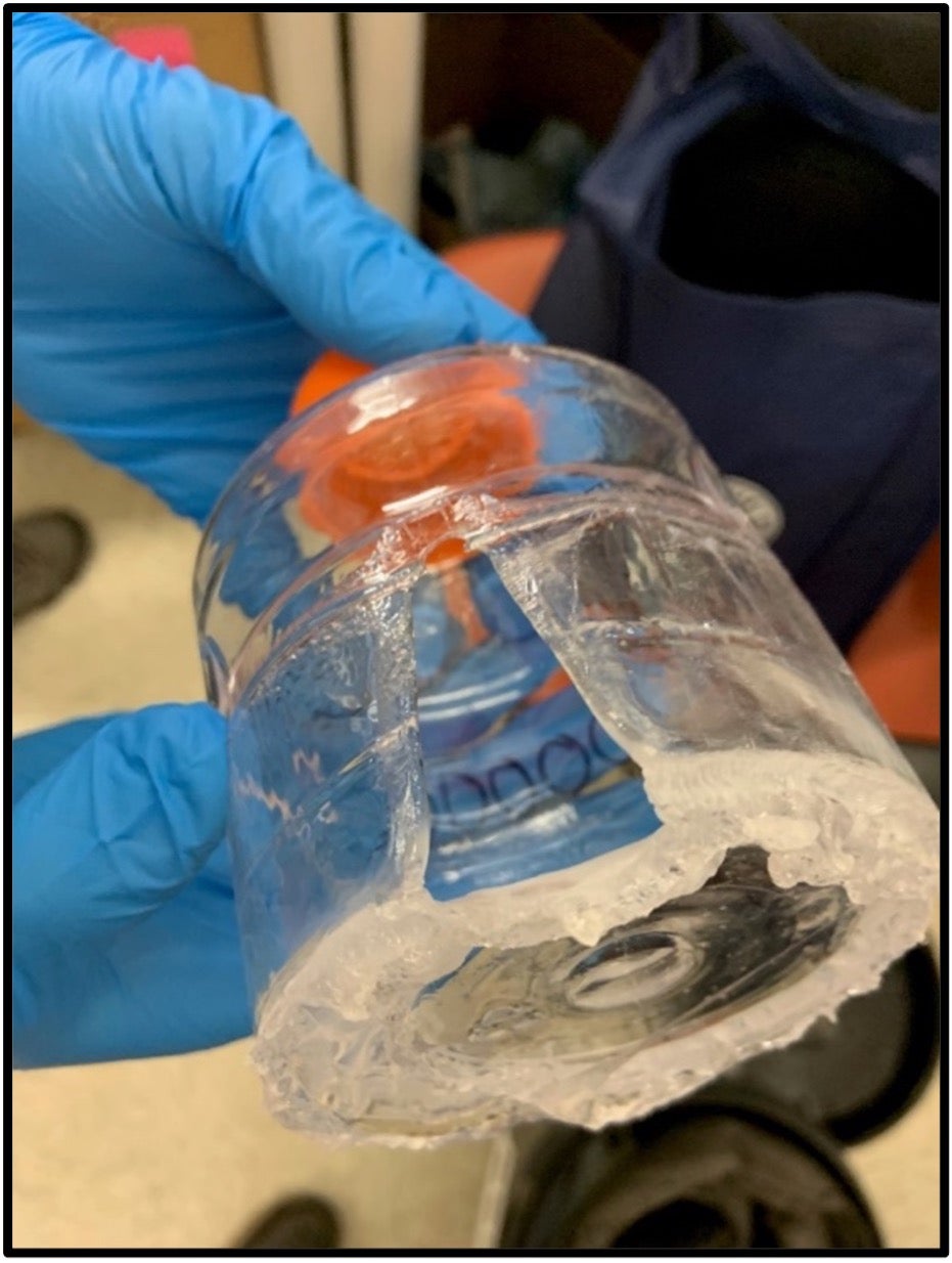 Gloved hands holding a bottle that was compromised and deteriorated from improper chemical storage.